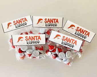 Pode incluir: Quatro sacos de plástico transparentes cheios de beijos de doces vermelhos e brancos. Cada saco tem uma etiqueta branca com uma ilustração de Papai Noel vermelha e o texto "Santa Kisses".