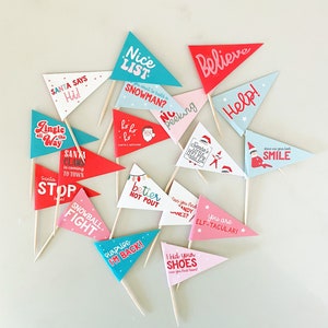 May include: A set of 12 festive Christmas themed cupcake toppers. The toppers are printed on cardstock and feature a variety of holiday sayings, including "Santa Says Hi!" and "Jingle All The Way".