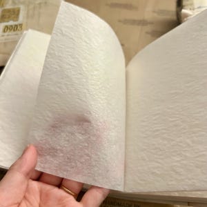 May include: A white, textured, handmade journal with the text "HANDMADE BY REMARKCREATIONS" printed on the bottom right corner.
