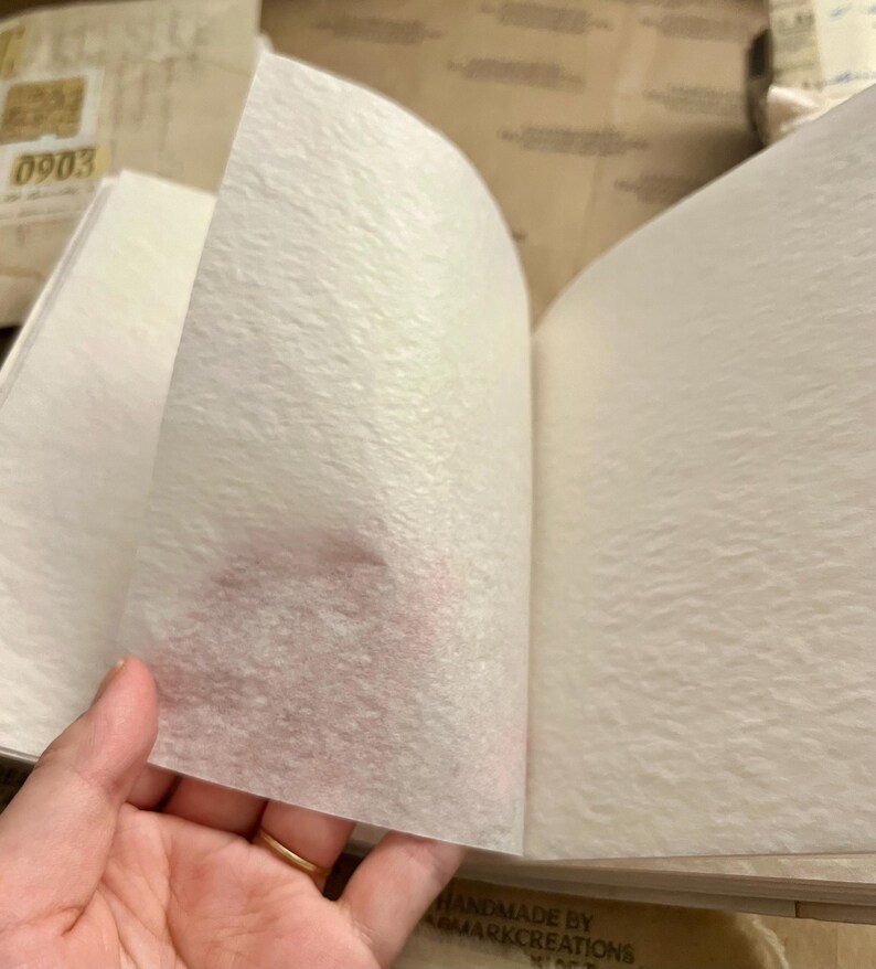 May include: A white, textured, handmade journal with the text "HANDMADE BY REMARKCREATIONS" printed on the bottom right corner.