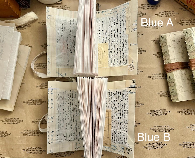 May include: Two stacks of blank, cream-colored paper journals with handwritten text on the pages. The journals are labeled "Blue A" and "Blue B" on brown paper.