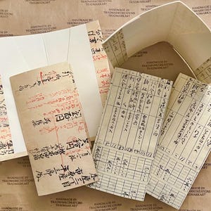 May include: A collection of vintage paper documents with handwritten Japanese text and numbers. The documents are folded and have a worn, aged appearance. Some of the documents are on a gridded background.