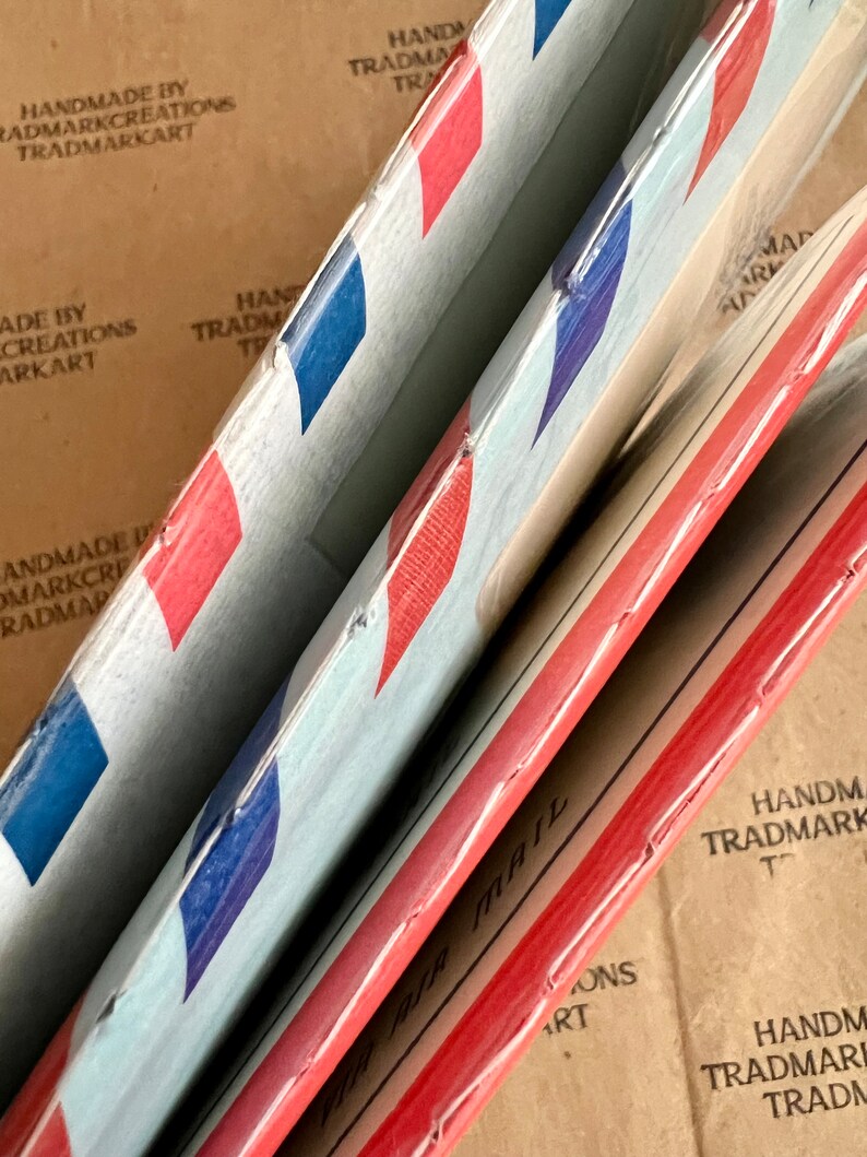 May include: Three red, white, and blue air mail envelopes stacked on top of each other. The envelopes are made of paper and have a red, white, and blue striped pattern. The envelopes are labeled "Air Mail" in black lettering.