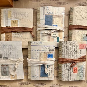 Peut inclure: Une collection de huit petits journaux faits à la main avec des couvertures brunes et blanches. Les journaux sont liés avec un ruban brun et blanc. Les couvertures sont décorées de divers éléments éphémères, notamment des timbres, des billets et des notes manuscrites.