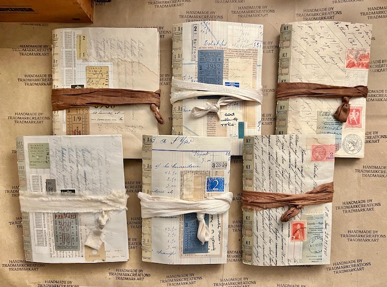 May include: A collection of eight small, handmade journals with brown and white covers. The journals are tied with brown and white ribbon. The covers are decorated with various ephemera, including stamps, tickets, and handwritten notes.