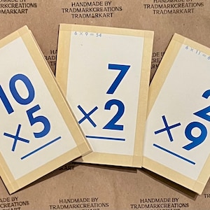 May include: Three wooden cards with blue numbers and multiplication problems. The cards are labeled "Handmade by Trademarkcreations Trademarkart". The problems are 10 x 5, 7 x 2, and 2 x 9.