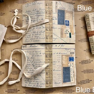 May include: Two vintage journals with brown paper covers and white ribbon ties. The journals are open to reveal pages filled with handwritten notes, stamps, and ephemera. The text on the pages includes "Blue A" and "Blue B".