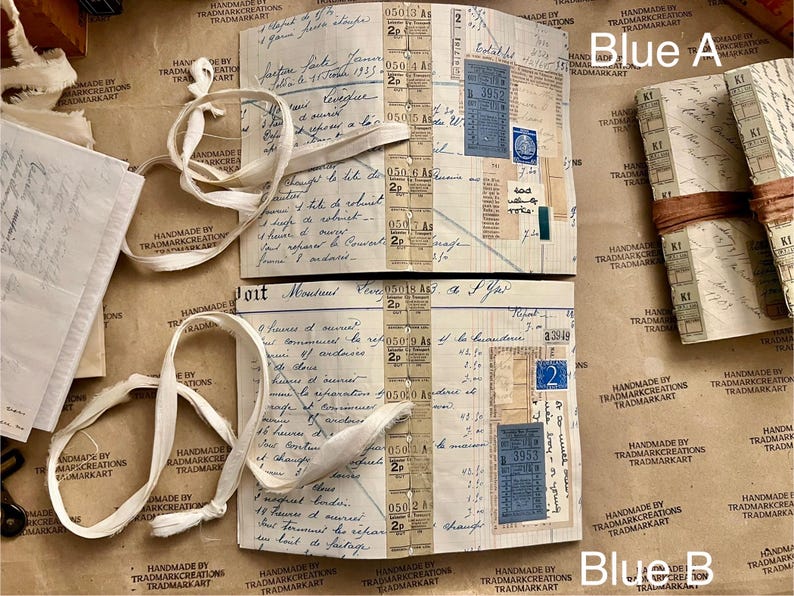 May include: Two vintage journals with brown paper covers and white ribbon ties. The journals are open to reveal pages filled with handwritten notes, stamps, and ephemera. The text on the pages includes "Blue A" and "Blue B".
