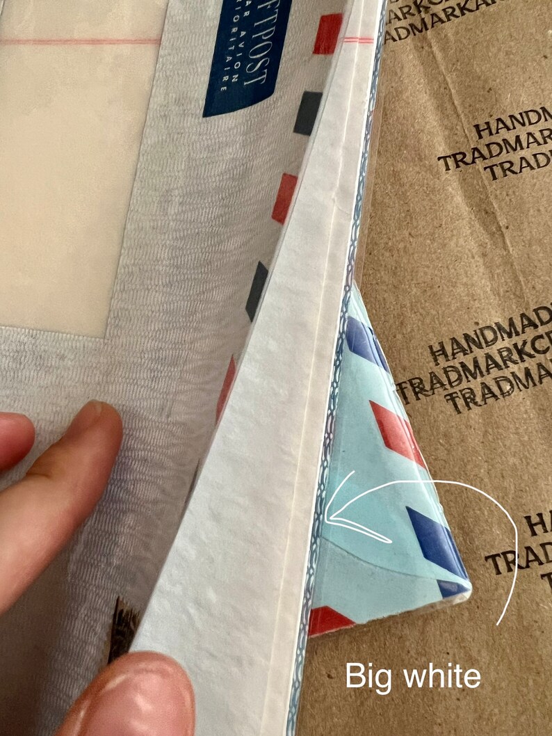 May include: A close-up of a white envelope with a blue and red patterned envelope underneath. The text "FTPOST" is visible on the white envelope. The text "HANDMAD TRADMARKC TRADMA" is visible on the brown envelope.