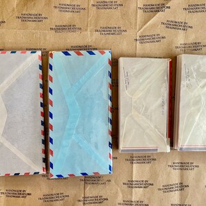 May include: A stack of five white and blue envelopes with red and blue stripes. The envelopes are made of paper and have a clear plastic window.