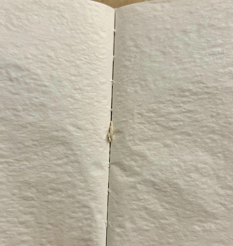 May include: A close-up of a white book with a visible seam down the center. The seam is slightly open, revealing a small piece of white paper.