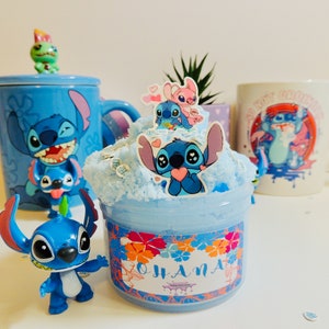 May include: Blue and white ceramic mug with a cartoon Stitch character design. The mug is next to a blue and white slime jar with a Stitch character sticker on the front. The slime jar has a floral design with the word "Ohana" on the front.
