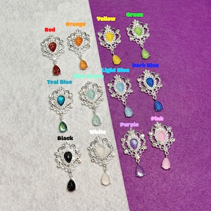 May include: Assortment of teardrop gem brooches in various colors, including red, orange, yellow, green, light blue, dark blue, teal blue, pink, purple, white, and black. Each brooch features a silver filigree design with a teardrop-shaped gem.