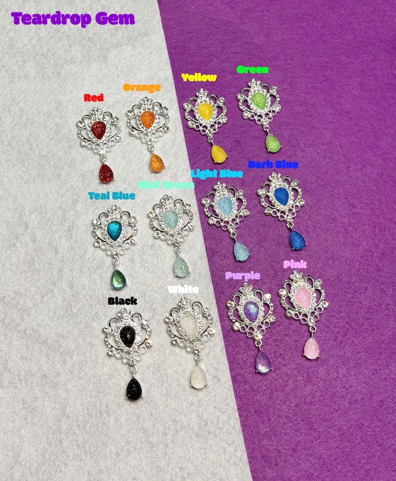 May include: Assortment of teardrop gem brooches in various colors, including red, orange, yellow, green, light blue, dark blue, teal blue, pink, purple, white, and black. Each brooch features a silver filigree design with a teardrop-shaped gem.