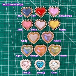 May include: Assortment of heart-shaped gem embellishments with pearl trim in various colors, including blue, red, light purple, pink, white, yellow, purple, aqua, orange, green, and clear.