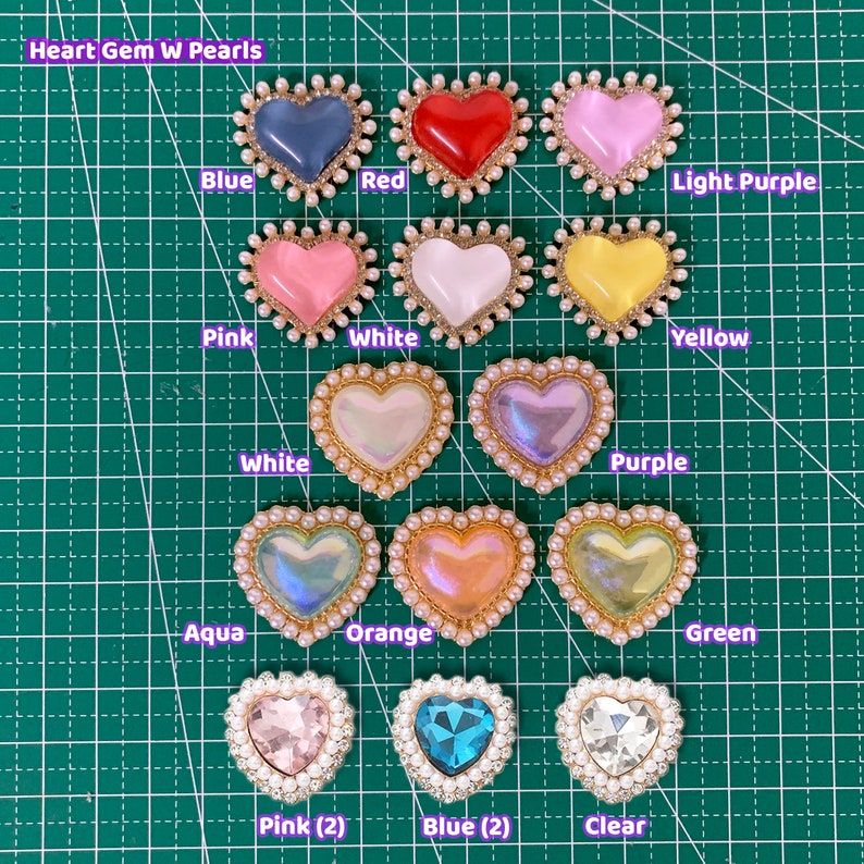 May include: Assortment of heart-shaped gem embellishments with pearl trim in various colors, including blue, red, light purple, pink, white, yellow, purple, aqua, orange, green, and clear.