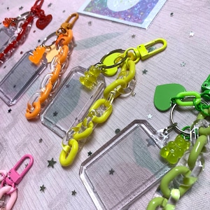 May include: Four colorful keychains with clear plastic frames and gummy bear charms. The keychains are made of plastic chain links in orange, yellow, green, and pink.
