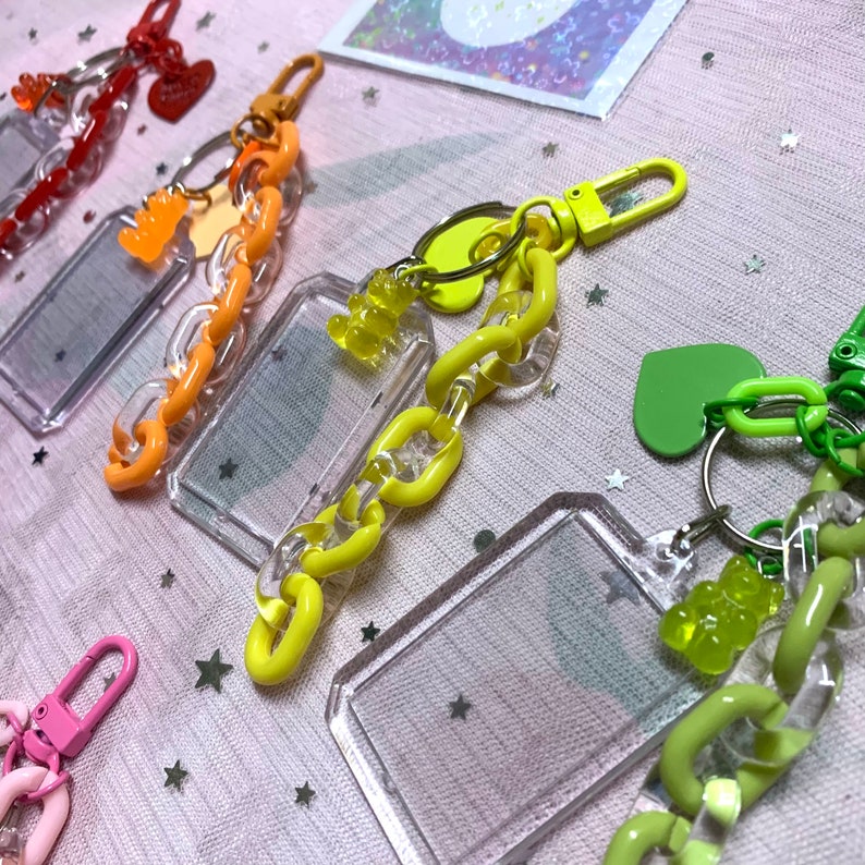 May include: Four colorful keychains with clear plastic frames and gummy bear charms. The keychains are made of plastic chain links in orange, yellow, green, and pink.