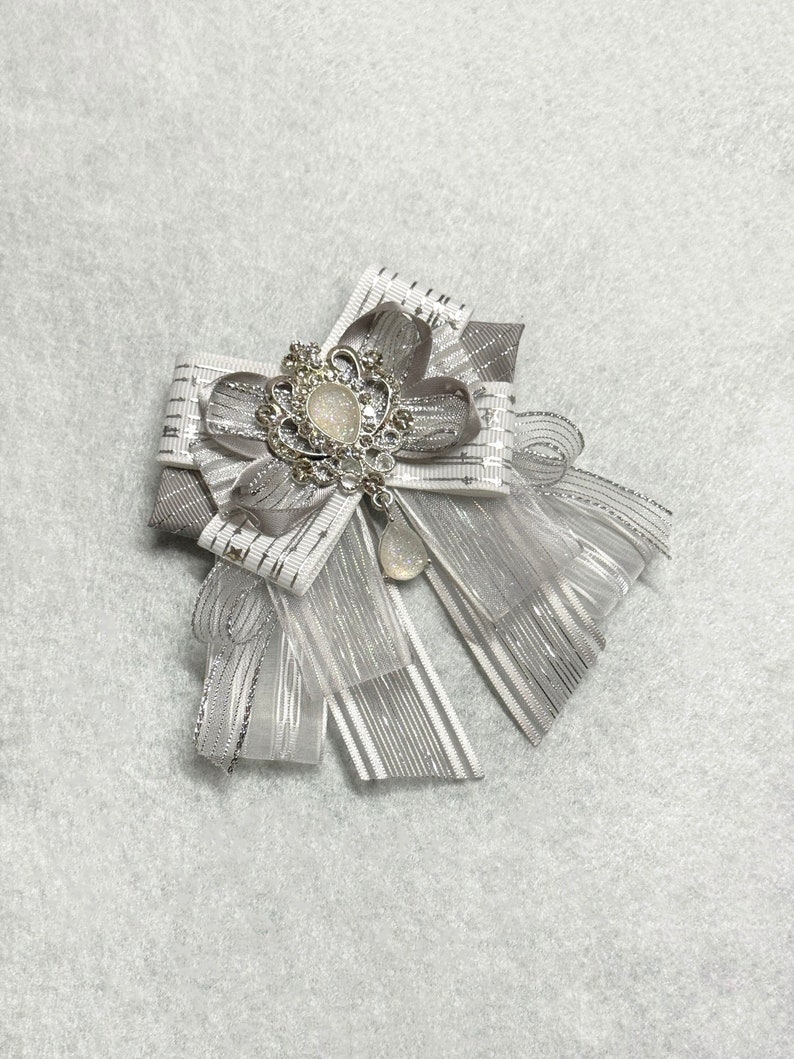 May include: A silver and white bow with a sparkly rhinestone embellishment. The bow is made of ribbon and tulle.