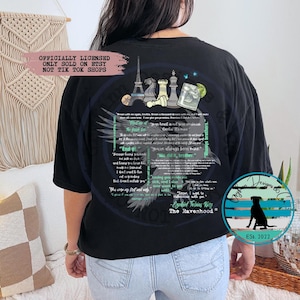 Peut inclure: T-shirt noir avec un imprimé graphique d'un corbeau aux ailes déployées, un échiquier, un verre de vin et la tour Eiffel. Le texte "The Ravenhood" et "Engraved Tales King" est imprimé sur le t-shirt. Le texte "Officially Licensed, Only Sold on Etsy, Not Tik Tok Shops" est imprimé en haut du t-shirt.