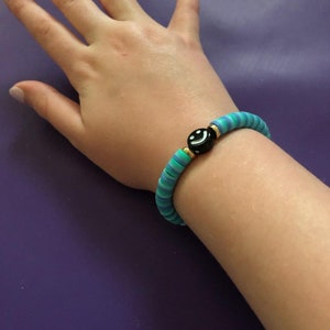 May include: A turquoise and blue striped bracelet with a black smiley face bead.