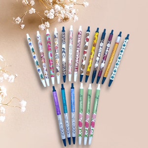 May include: A collection of 20 colorful pens with various designs and patterns. The pens have black ink and white barrels with different designs, including cacti, watermelon, leopard print, and floral patterns. Some pens have text on them, such as "MOM" and "#TRUECRIMEJUNKIE".