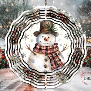 Op de afbeelding: Een decoratief, gelaagd metalen sneeuwmanornament. De sneeuwman draagt een bruine hoge hoed, een geruite sjaal en heeft takken als armen. Het ornament heeft een winterse achtergrond met sneeuwvlokken en groen. Het ornament hangt aan een ketting.