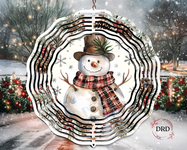 Op de afbeelding: Een decoratief, gelaagd metalen sneeuwmanornament. De sneeuwman draagt een bruine hoge hoed, een geruite sjaal en heeft takken als armen. Het ornament heeft een winterse achtergrond met sneeuwvlokken en groen. Het ornament hangt aan een ketting.