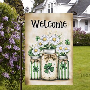 May include: A garden flag with the word "Welcome" in black script. The flag features three mason jars filled with daisies and shamrocks. The jars have green and white stripes and are tied with brown ribbons. The background is a light beige.