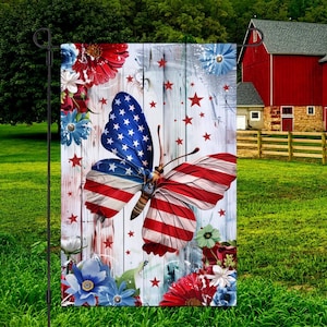 May include: A garden flag featuring a butterfly with wings designed as the American flag, set against a rustic wooden background. Red, white, and blue floral accents and stars complete the patriotic theme.