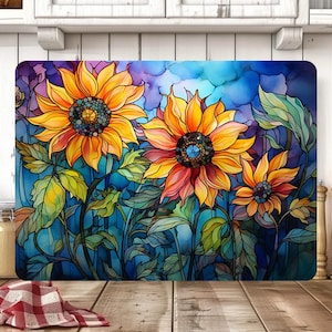 May include: Rectangular chopping board with a watercolour design of sunflowers. The sunflowers have yellow and orange petals with dark centres, set against a blue and purple background. Green leaves and stems complete the floral arrangement.