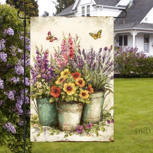 May include: A garden flag with a watercolour illustration of vibrant flowers in metal buckets, with butterflies. The flowers include purple, red, yellow, and white blooms. The flag is designed for outdoor use.