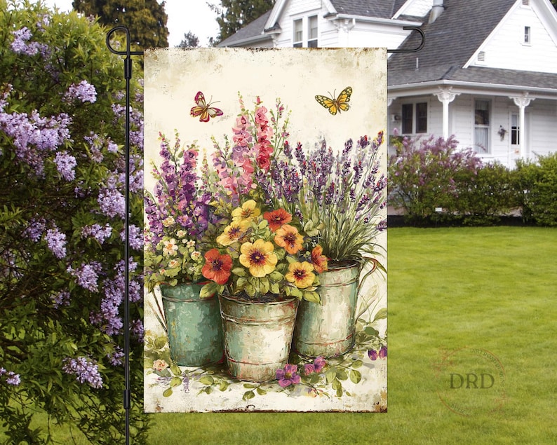 May include: A garden flag with a watercolour illustration of vibrant flowers in metal buckets, with butterflies. The flowers include purple, red, yellow, and white blooms. The flag is designed for outdoor use.