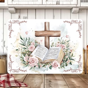 May include: Rectangular cutting board featuring a watercolor design with a wooden cross, an open book, and pink roses. The design includes green leaves, hearts, and a decorative border. The board rests on a wooden surface.