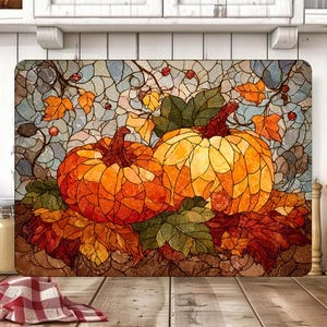 Könnte beinhalten: Rechteckiges Schneidebrett mit einem Design im Stil von Buntglas, das zwei orangefarbene Kürbisse zeigt, umgeben von Herbstblättern in Rot, Orange und Grün. Der Hintergrund hat ein Mosaikmuster mit Blau, Grau und Weiß.