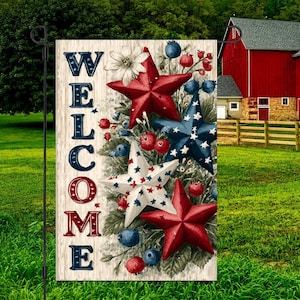 May include: A garden flag with the word "WELCOME" in red, white, and blue lettering. The flag features red, white, and blue stars, berries, and flowers. The flag is displayed on a black metal stand in a grassy yard.