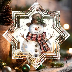 Op de afbeelding: Een kerstversiering met een aquarel sneeuwpop met een bruine hoge hoed en een geruite sjaal. De sneeuwpop staat in een stervormige lijst met een gouden geometrisch ontwerp en wintergroen. Een feestelijke vakantieversiering.