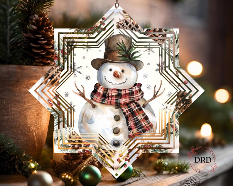 Op de afbeelding: Een kerstversiering met een aquarel sneeuwpop met een bruine hoge hoed en een geruite sjaal. De sneeuwpop staat in een stervormige lijst met een gouden geometrisch ontwerp en wintergroen. Een feestelijke vakantieversiering.