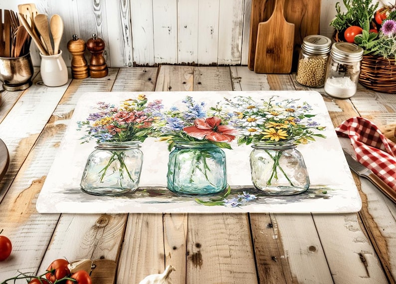 May include: A rectangular kitchen mat featuring a watercolor painting of three glass mason jars filled with colorful wildflowers. The jars are set against a white background, with a rustic wooden table in the foreground.