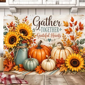 May include: A rectangular decorative sign featuring a rustic white wood background with the text Gather TOGETHER Grateful Hearts. The design includes yellow sunflowers in a blue jar, orange and white pumpkins, and autumn leaves in shades of red.