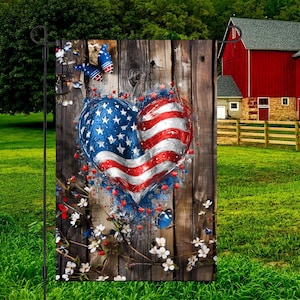 May include: A patriotic garden flag featuring a heart-shaped American flag design on a rustic wooden background. The flag is adorned with red, white, and blue colors, with stars and stripes. Butterflies and flowers add decorative elements.
