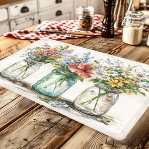 May include: Rectangular kitchen mat featuring a watercolor design of three mason jars filled with colorful wildflowers. The mat has a white border and is set on a rustic wooden table. The flowers include red, pink, blue, and yellow blooms.