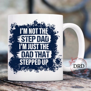May include: White ceramic mug with a blue and white design. The text on the mug reads "I'm not the step dad I'm just the dad that stepped up".