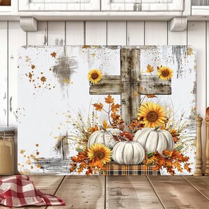 May include: A rectangular cutting board featuring a rustic wooden cross, sunflowers, white pumpkins, and autumn leaves. The design has a white background with brown and gold accents, creating a fall harvest theme.