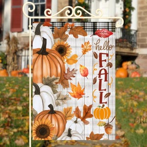 May include: A decorative fall garden flag featuring pumpkins, sunflowers, and autumn leaves in shades of orange, white, and brown. The flag has the words "hello FALL" printed on it. The flag is displayed on a white metal stand.
