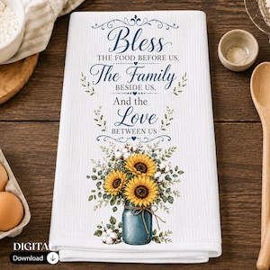 Può includere: Un canovaccio bianco a nido d'ape con testo blu in corsivo che recita Bless THE FOOD BEFORE US, The Family BESIDE US, And the Love BETWEEN US, con un disegno di girasoli e rami di cotone in un barattolo di vetro blu.