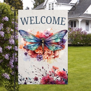 Puede incluir: Una bandera de jardín de bienvenida con un diseño de acuarela de una mariposa con alas azules, moradas y verdes. La mariposa está rodeada de flores rosas, rojas y blancas. La bandera tiene la palabra "WELCOME" impresa en letras azules.