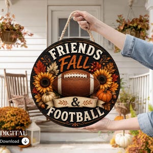 May include: A round wooden sign featuring a brown football in the centre, surrounded by sunflowers, orange pumpkins, and autumn leaves. The text reads "FRIENDS FALL & FOOTBALL" in white and orange lettering. The sign hangs from a thick rope.