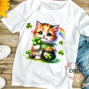 May include: White t-shirt with a cartoon image of a cute orange and white cat holding a pot of gold and a shamrock. The cat is surrounded by shamrocks and a rainbow.