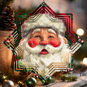 Puede incluir: Un adorno navide&ntilde;o en forma de estrella con Pap&aacute; Noel con barba blanca, mejillas rojas y gafas doradas. El adorno tiene un dise&ntilde;o festivo con patrones geom&eacute;tricos rojos, verdes y dorados. El adorno cuelga frente a un fondo borroso con decoraciones navide&ntilde;as.